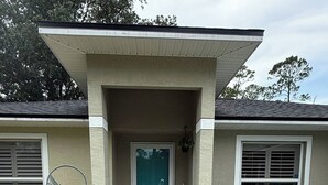Una casa con porche cubierto, puerta y mobiliario exterior con sillas y macetas.