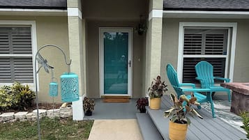 A house with a covered porch, a door, and outdoor seating with chairs and planters.