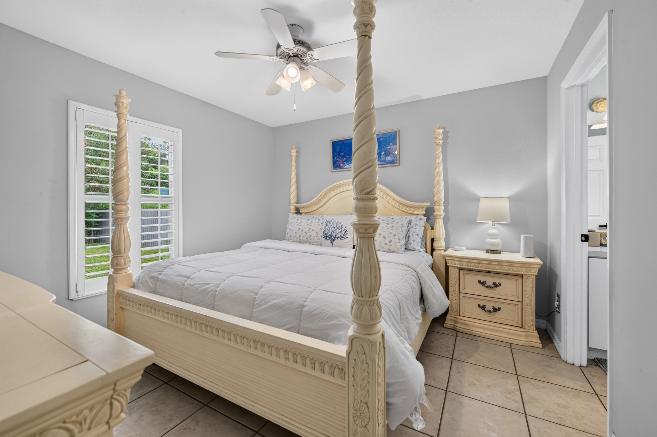 A four-poster bed with a ceiling fan, a bedside table with a lamp, and a nightstand with a lamp.
