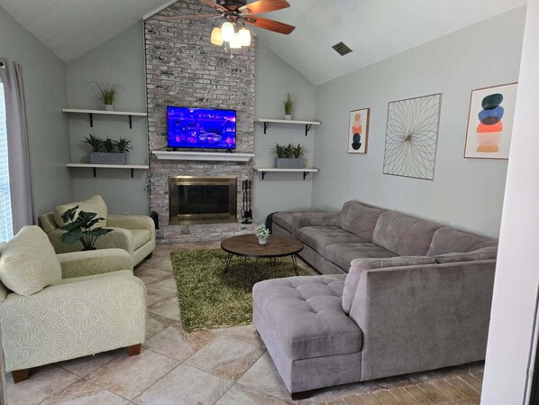 A living room with a stone fireplace, a flat-screen TV, and a grey sofa.