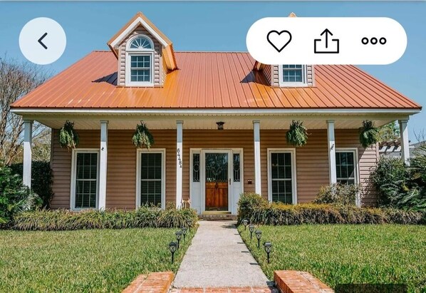 Ein zweigeschossiges Haus mit rotem Metalldach, einer Veranda mit Säulen und einer kleinen Garage.