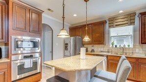 Una cocina con armarios de madera, electrodomésticos de acero inoxidable, encimera de granito e iluminación colgante.