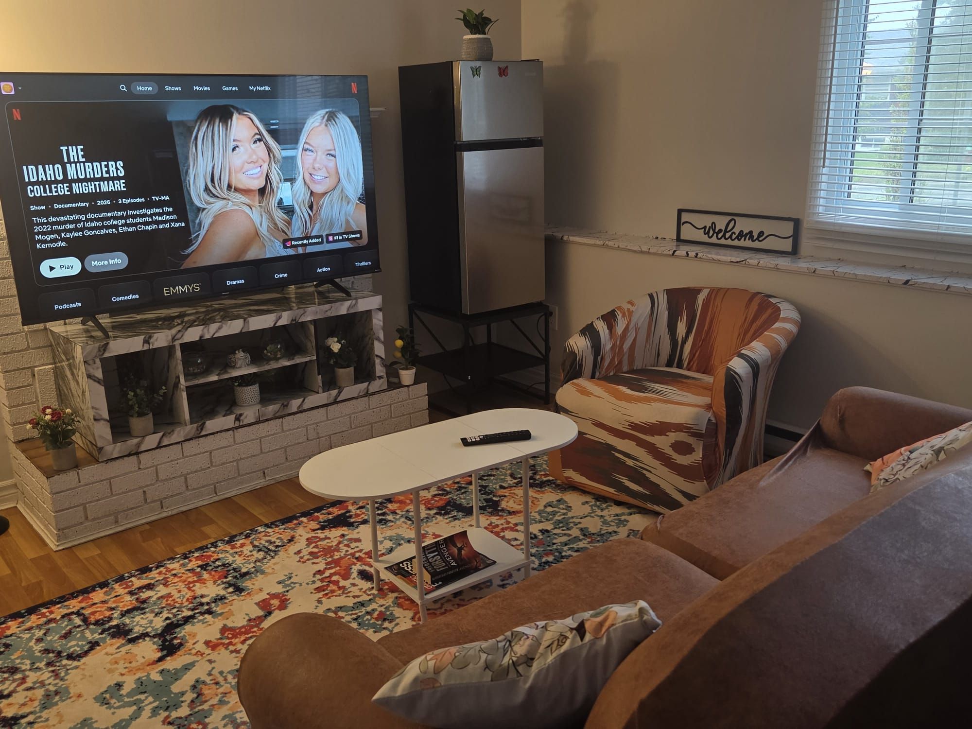 Un salon avec un téléviseur à écran plat diffusant un documentaire, une cheminée, un canapé, une table basse et un panneau décoratif accueillant les visiteurs.