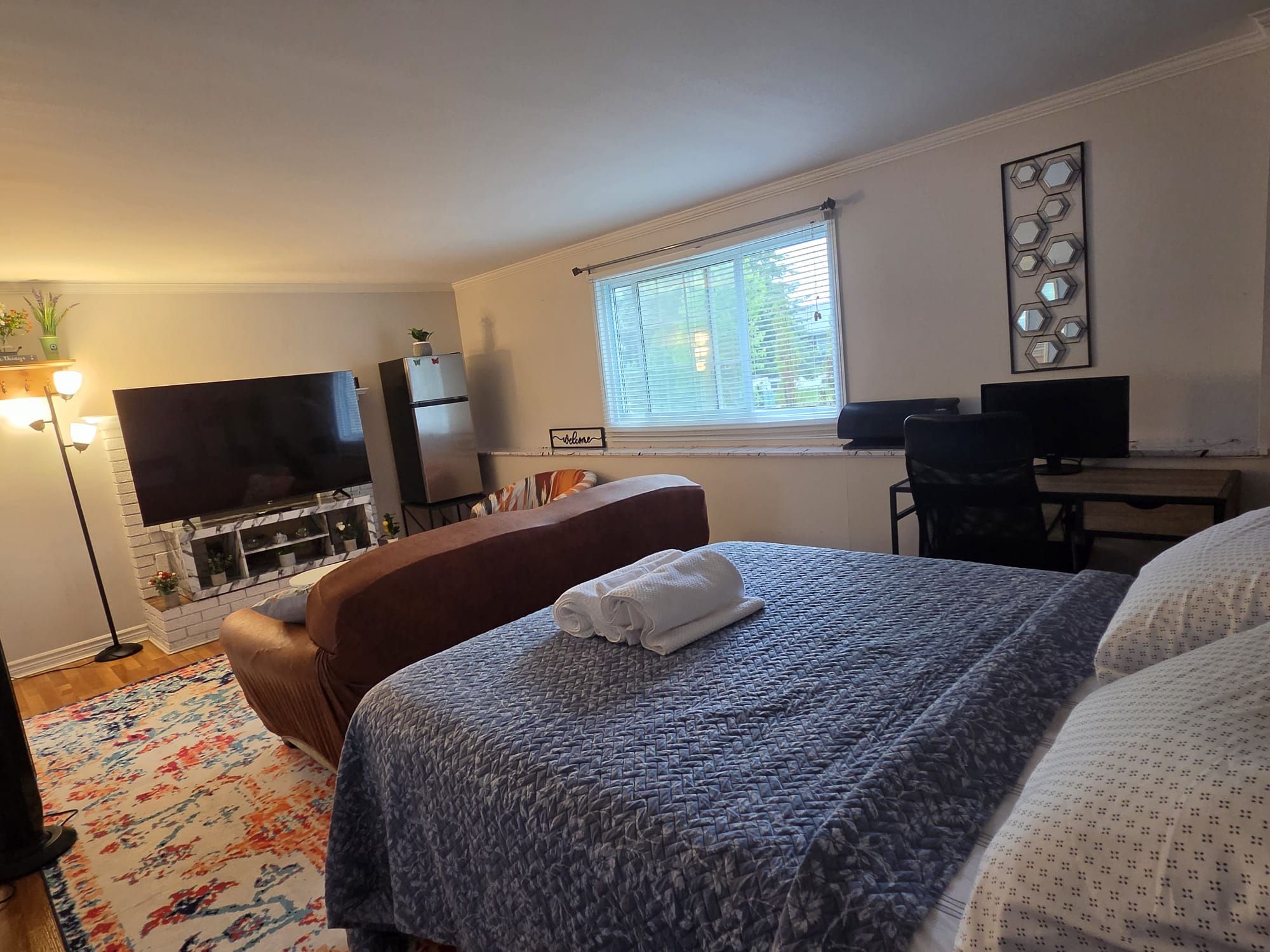 A hotel room with a bed, a desk, a television, and a refrigerator.