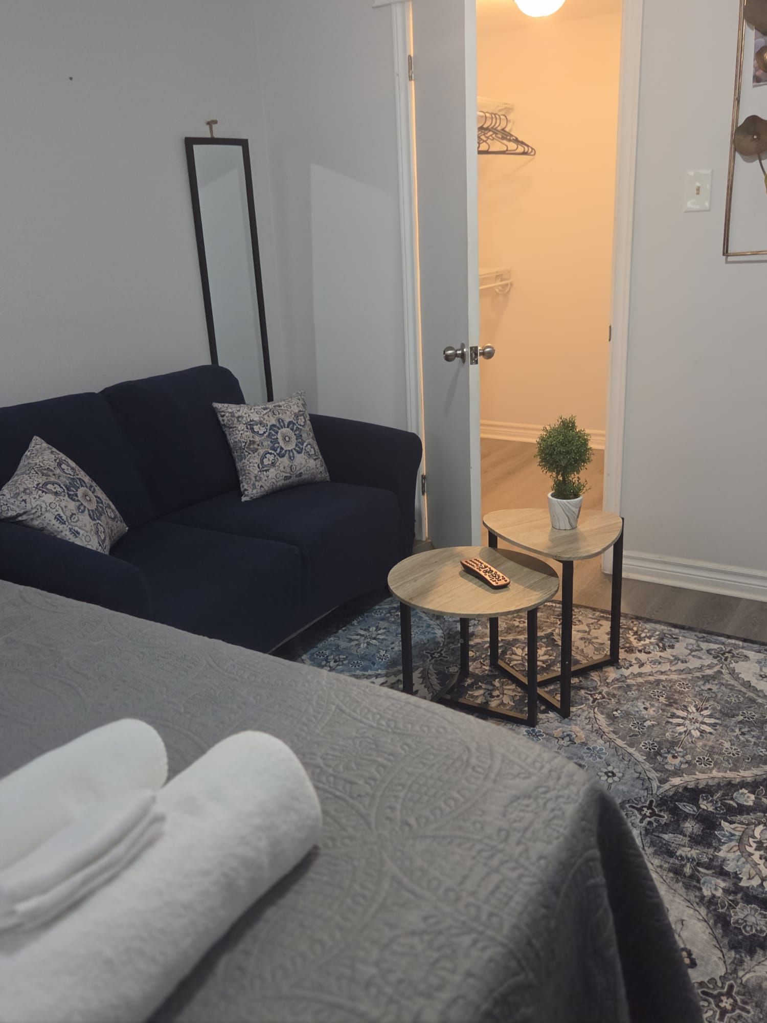 A room with a bed, a dark blue sofa, a small round table with a plant, and a mirror on the wall.