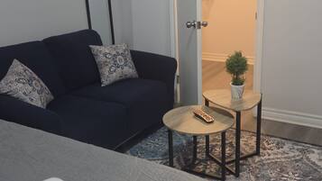 A room with a bed, a dark blue sofa, a small round table with a plant, and a mirror on the wall.