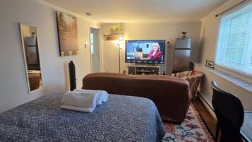 Una habitación de hotel con cama, televisión, refrigerador y ventana con persianas.