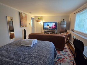 A hotel room with a bed, a television, a refrigerator, and a window with blinds.