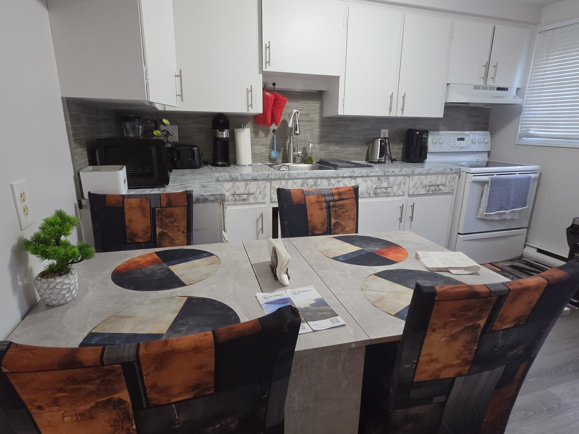 Una cocina moderna con armarios blancos, encimera de mármol y mesa de comedor con un diseño geométrico original.