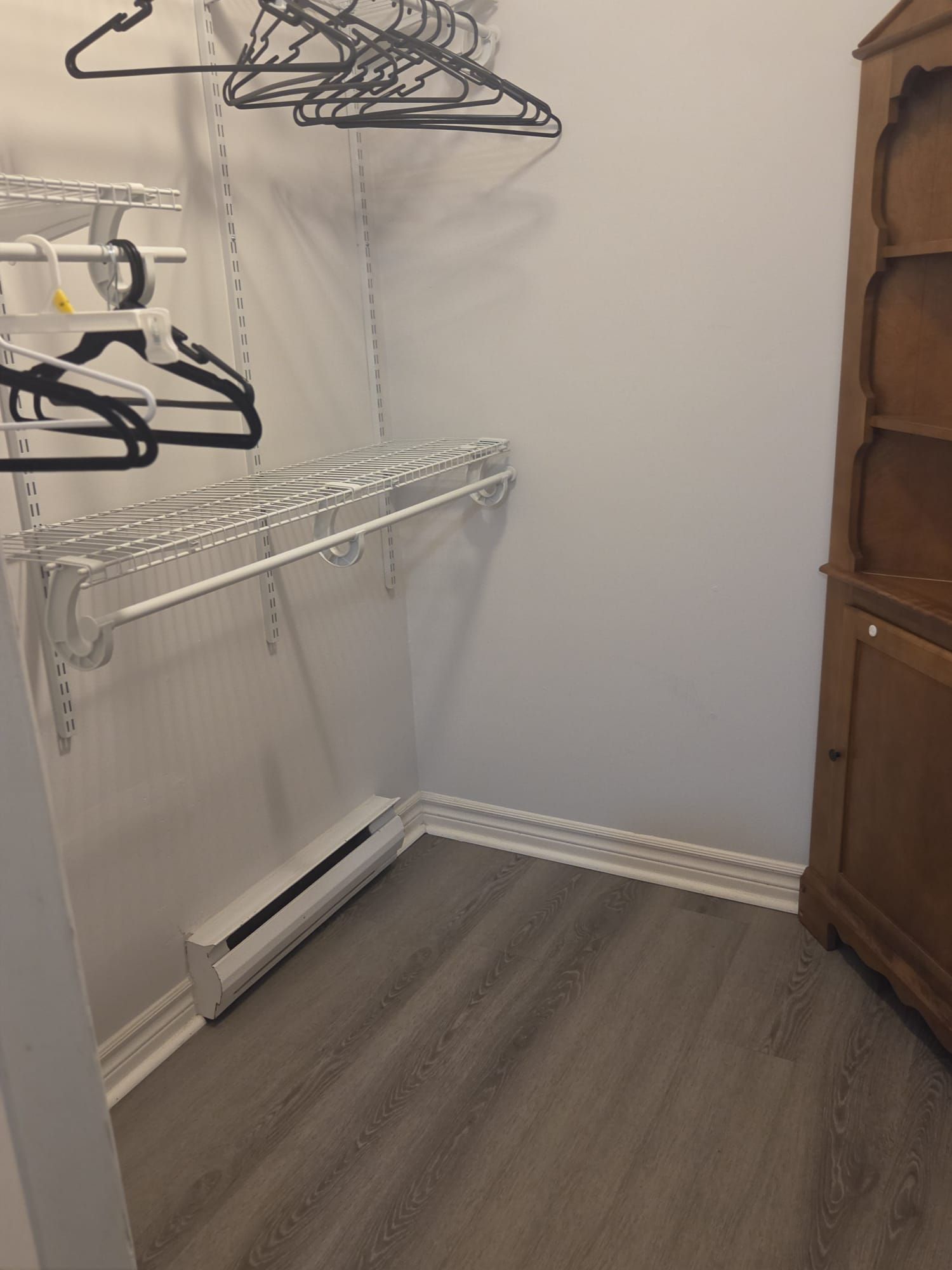 A corner of a room with a white radiator, a metal shelf unit, and a wooden cabinet.