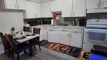 A modern kitchen with white cabinets, a marble countertop, a stove, and a dining area with a table and chairs.