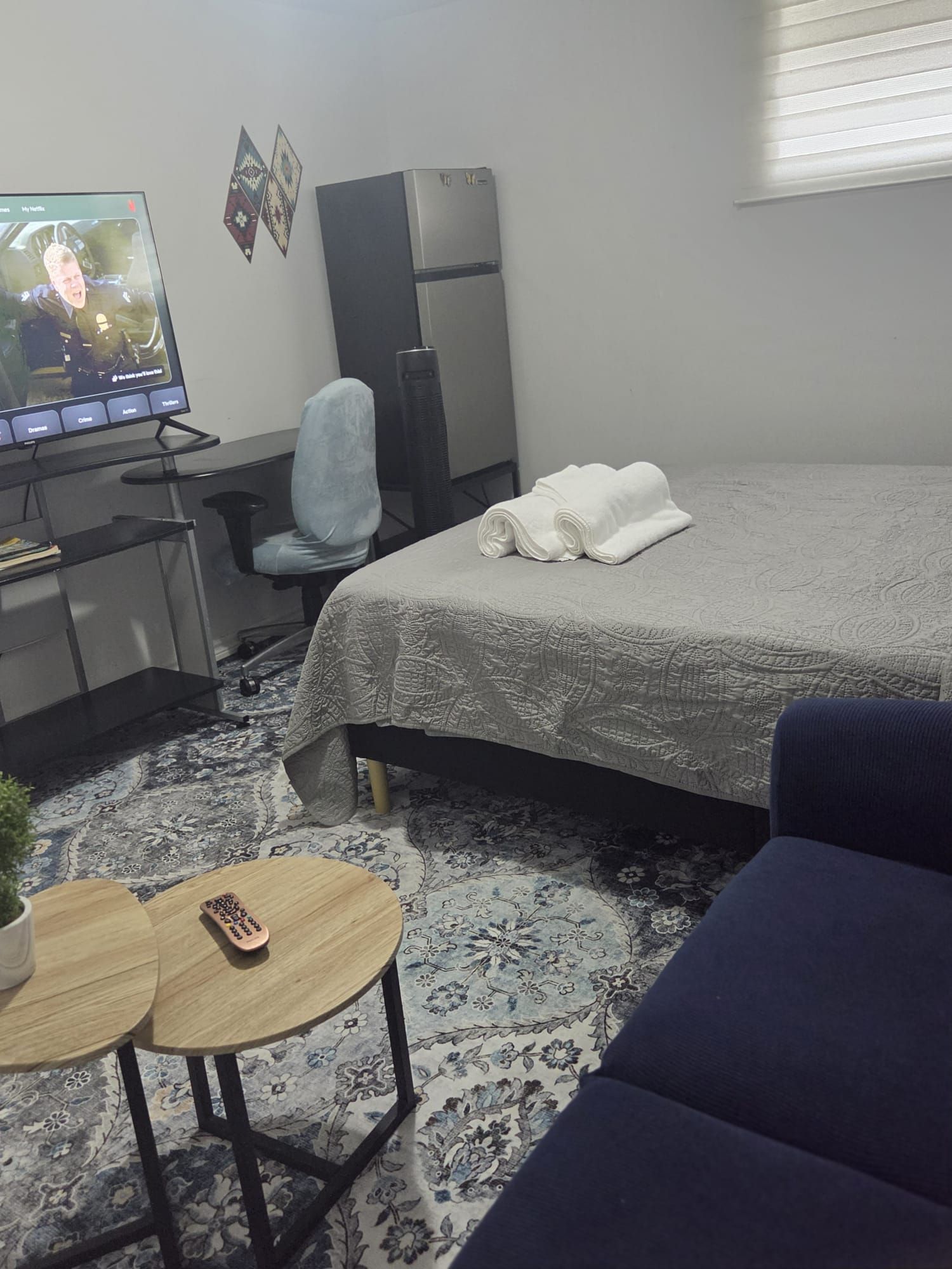 Une chambre d’hôtel avec un lit, un bureau avec un ordinateur, une chaise, une petite table avec une plante et un canapé bleu.