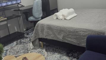 Une chambre d’hôtel avec un lit, un bureau avec un ordinateur, une chaise, une petite table avec une plante et un canapé bleu.