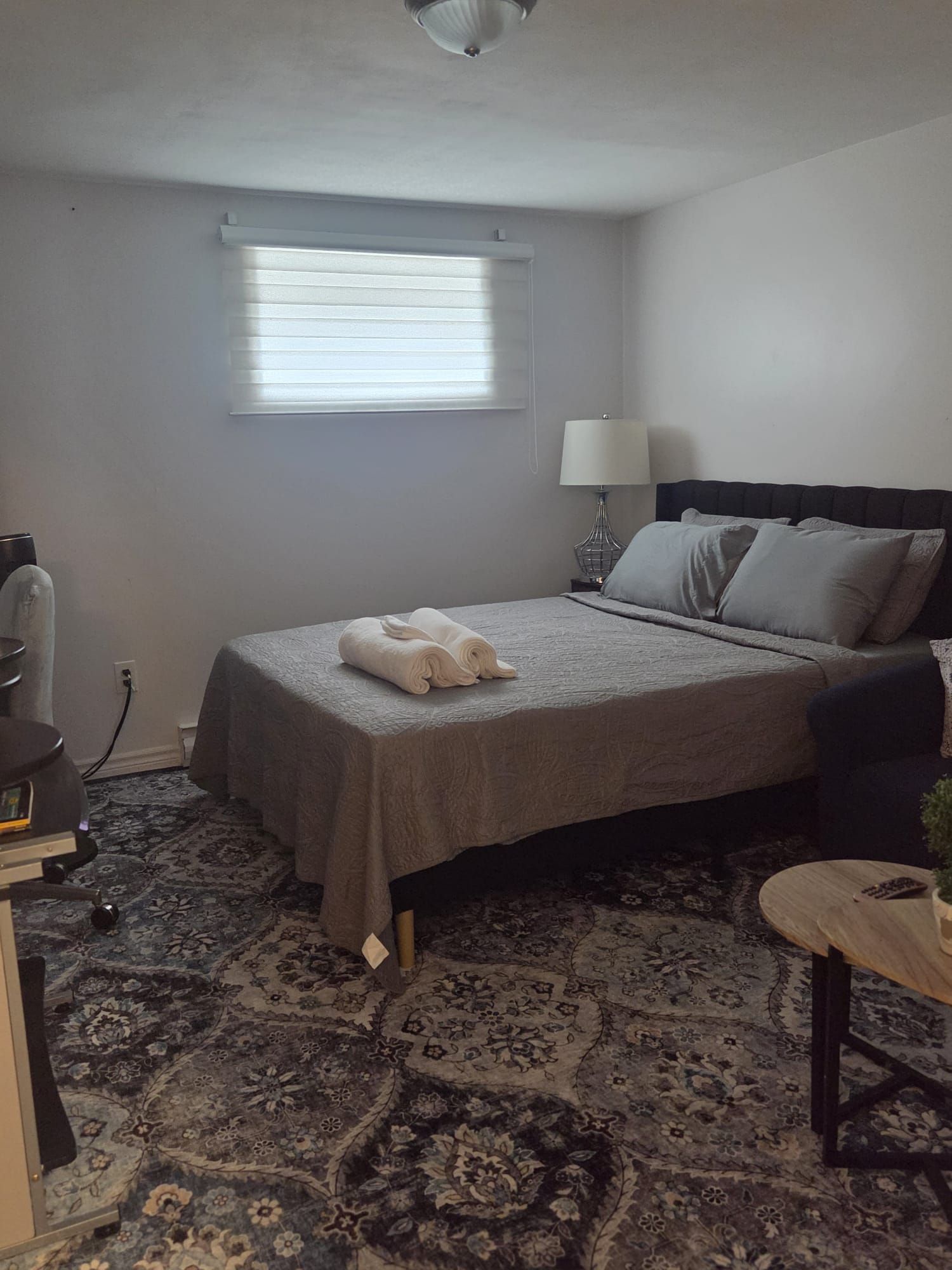 A hotel room with a bed, a desk, a lamp, and a small table.