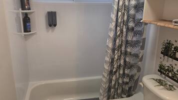 A bathroom with a bathtub, toilet, and a window above the bathtub.