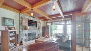 A spacious living room with a stone fireplace, leather furniture, and large windows offering a view of the outdoors. - Luxe Family Home on Orange Lake w/ Private Dock! (Newburgh)