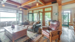 A spacious living room with a large wooden ceiling, a leather sofa, a wooden armchair, and a coffee table. - Luxe Family Home on Orange Lake w/ Private Dock! (Newburgh)
