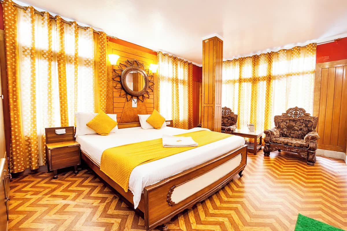 A hotel room with a large bed, wooden headboard, a nightstand, a chair, a mirror, and a window with curtains.
