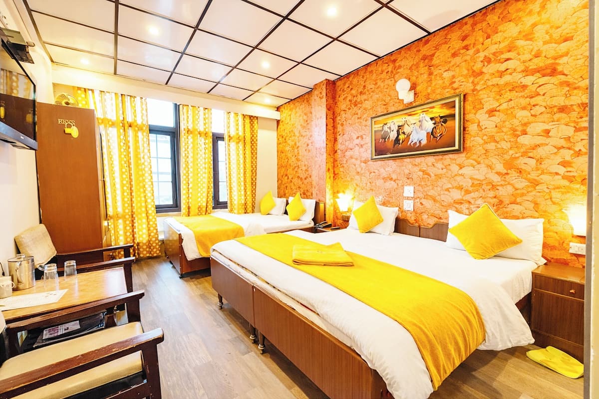 A hotel room with two beds, a wooden desk, a chair, a wardrobe, and a stone wall with a painting.