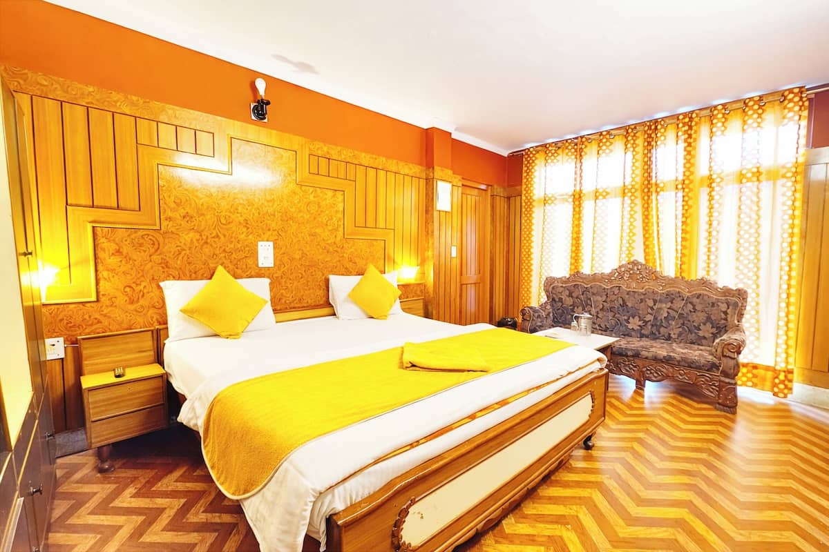 A hotel room with a large bed, a wooden nightstand, a sofa, and a patterned wall.