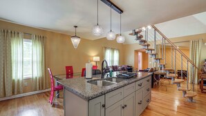 A kitchen with granite countertops, a central island, and a built-in sink. There are pendant lights above the island, a staircase with wooden steps, and a dining area with a red chair. - 11 Mi to Oneida Lake: Spacious Apt in Verona! (Verona)