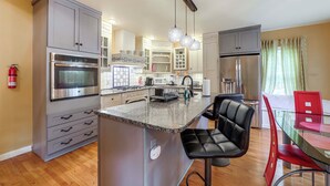 A modern kitchen with grey cabinets, stainless steel appliances, a central island with a black chair, and a dining area with red chairs. - 11 Mi to Oneida Lake: Spacious Apt in Verona! (Verona)