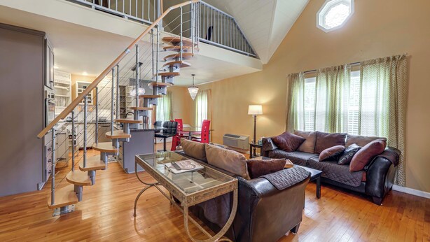 A spacious living area with a wooden staircase, a leather sofa, and a dining area with red chairs. - 11 Mi to Oneida Lake: Spacious Apt in Verona! (Verona)