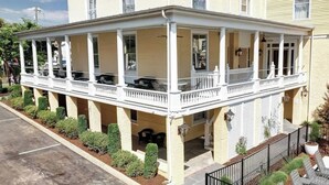 Un edificio a due piani con un portico coperto, diverse finestre e un piccolo giardino.