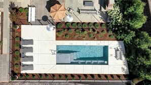 Vista aerea di una zona piscina su un tetto, con lettini, ombrelloni e una piscina.