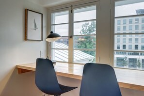 Een kamer met een groot raam, een bureau, twee stoelen en een hanglamp.