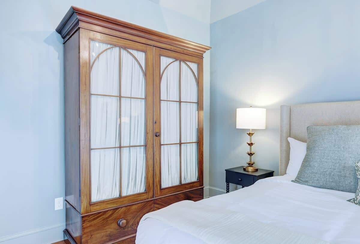 A bedroom with a bed, a nightstand with a lamp, and a wooden wardrobe.