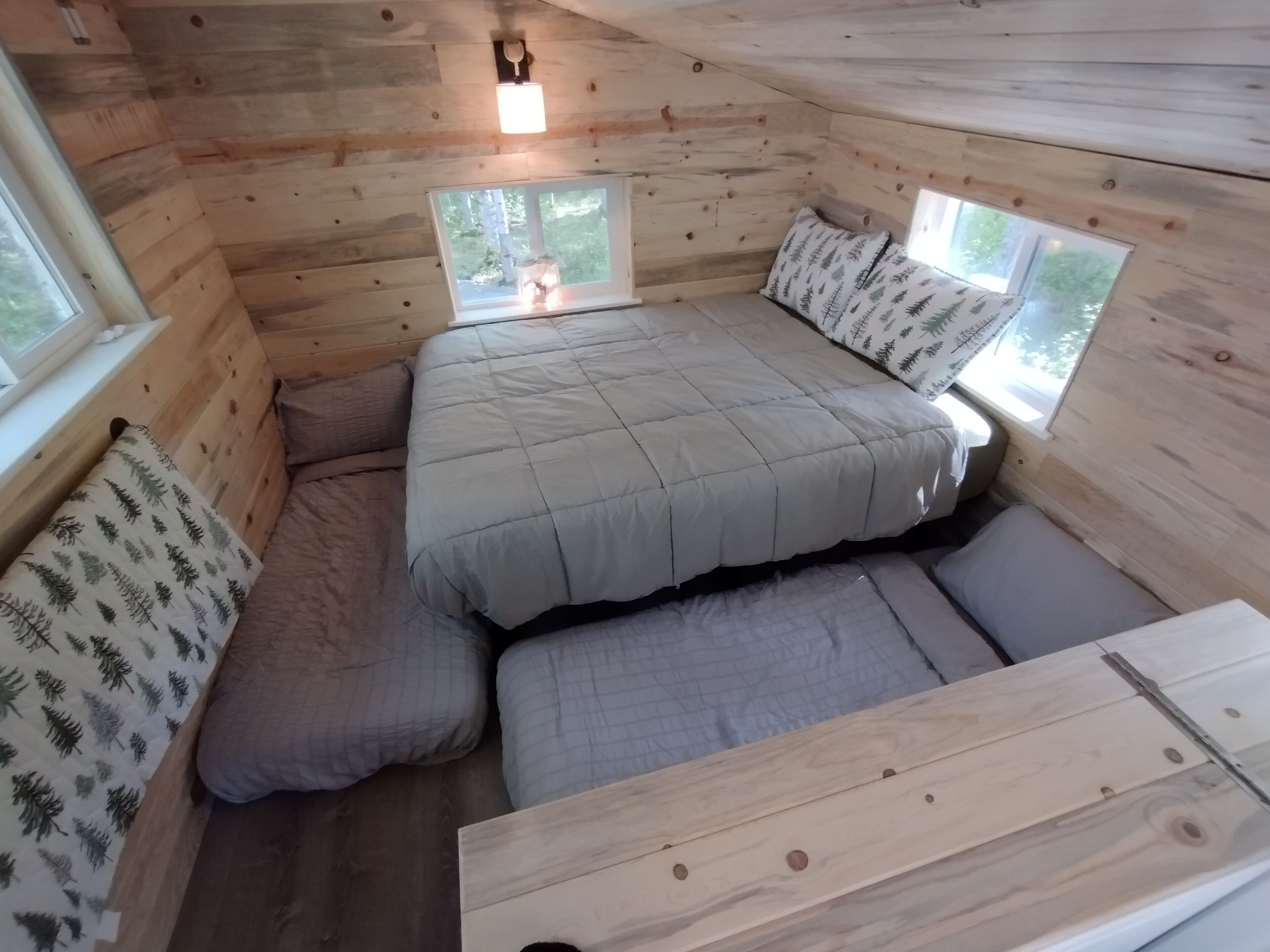 Een knus houten huisje met een bed, twee ramen en een kleine tafel.