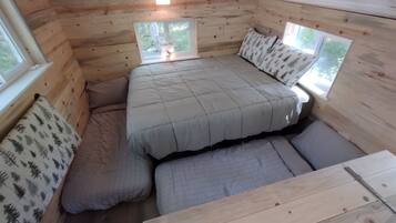 Een knus houten huisje met een bed, twee ramen en een kleine tafel.