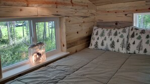 A cabin interior with a bed, a window with a view of greenery, and a hanging light fixture.