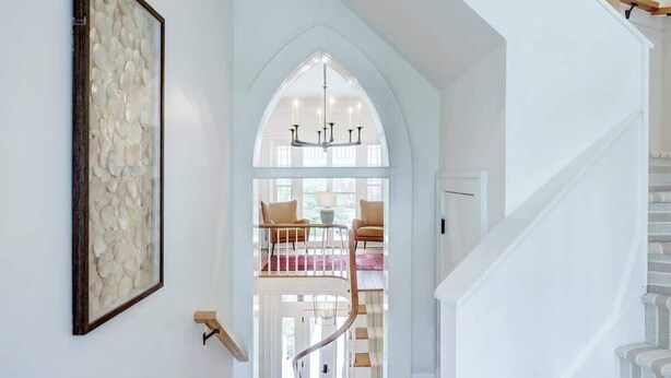 A staircase leading to a lofted area with a chandelier, a framed artwork on the wall, and a view of the outdoors.