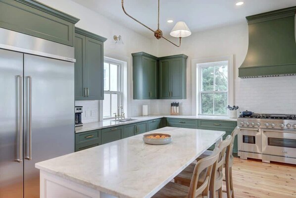 A kitchen with a marble island, stainless steel appliances, and green cabinetry.