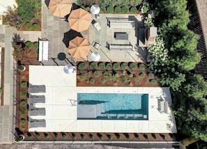 An aerial view of a rooftop pool area with sun loungers, umbrellas, and a small seating area. - Downtown King Room with Outdoor Fireplace (Charlottesville)