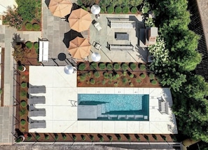 An aerial view of a rooftop pool area with lounge chairs, umbrellas, and a swimming pool.