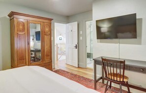 A bedroom with a bed, a wooden wardrobe, a desk with a chair, and a television mounted on the wall. - Historic Boutique Hotel with Pool (Charlottesville)