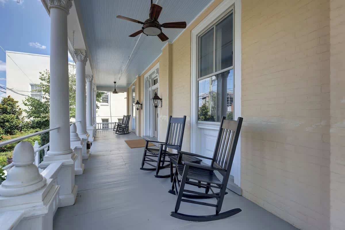 A covered porch with white columns, black rocking chairs, and a ceiling fan.
