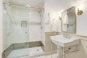 A bathroom with a glass-enclosed shower, a white sink, a mirror, and a towel rack.