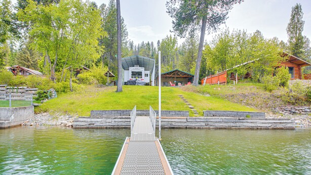 En brygga som leder fram till ett hus med en inglasad veranda, omgivet av träd och en gräsyta.