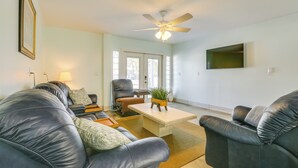 A living room with a sofa set, a coffee table, a ceiling fan, and a TV mounted on the wall. - Walk to Beach: Fort Meyers Home w/ Patio! (Fort Myers Beach)
