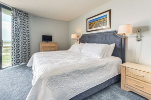 A hotel room with a large bed, a television, a desk, and a window with curtains.
