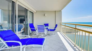 Enjoy stunning beach views from this spacious balcony with comfortable lounge chairs and a small table.
