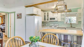 A kitchen with white cabinets, a wooden dining table, and a hanging light fixture.