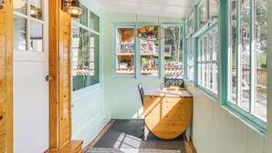 A narrow hallway with a wooden door, a small table with a chair, and a window with a view of a deck and outdoor furniture. - Salmon Return & Wildlife Roam: Ketchikan Getaway! (Ketchikan)