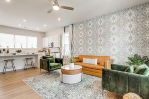 Una sala de estar moderna con un sofá verde, una mesa de centro redonda y una cocina al fondo.