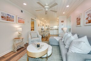 A spacious living room with a grey sofa, a round coffee table, and a ceiling fan. There are framed pictures on the walls and a dining area in the background. - Walk to Beach & Marsh: Condo in Murrells Inlet (Murrells Inlet)