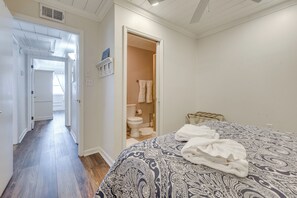 A bedroom with a patterned bedspread, a neatly folded towel, and a visible bathroom with a toilet and towel rack. - Walk to Beach & Marsh: Condo in Murrells Inlet (Murrells Inlet)
